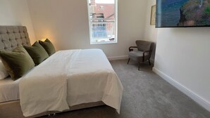 Un dormitorio con cama, una silla, un ventanal y un cuadro en la pared.