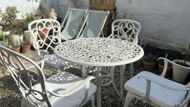 Un patio con una mesa metálica redonda y sillas blancas de metal.