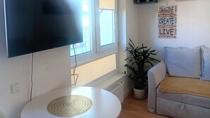 Een woonkamer met een flatscreen televisie aan de muur, een ronde witte tafel, een potplant, een bank met kussens en inspirerende muurkunst.