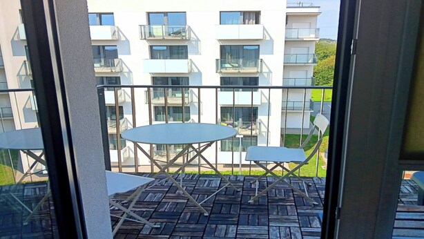 Een balkon met een houten vloer en twee witte tafels.