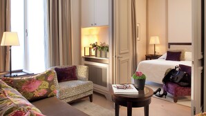 A hotel room with a bed, a sofa, a chair, a small table with a book and a plant, and a nightstand with a lamp. - Hôtel de l'Arcade (Paris)