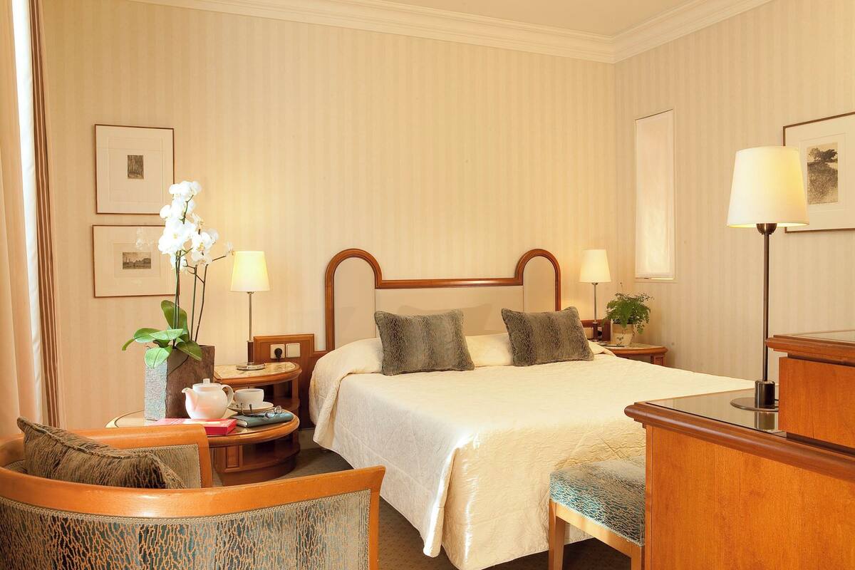 A hotel room with a bed, bedside tables, a chair, a desk, and a lamp.