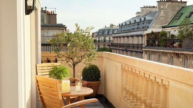 A balcony with a wooden chair and table, potted plants, and a view of Parisian buildings. - Hôtel de l'Arcade (Paris)