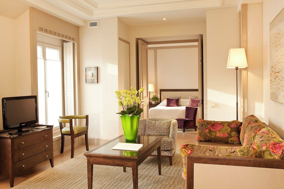 A hotel room with a bed, a desk with a computer, a chair, a sofa, and a lamp.
