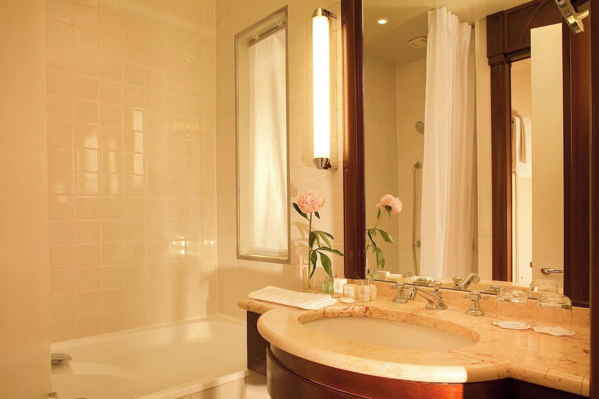 A bathroom with a bathtub, a sink with a marble countertop, and two mirrors.