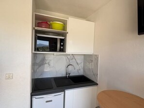 A compact kitchen with a sink, a microwave, and storage shelves.