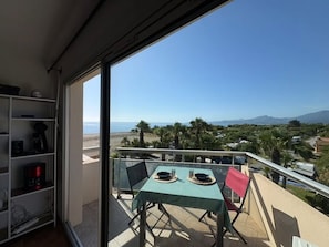 Un balcón con una mesa dispuesta para dos personas, con vistas a una playa y montañas a lo lejos.