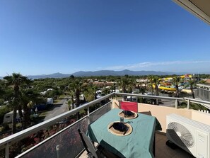 Ein Balkon mit Tisch, einem Ventilator und Blick auf einen Wasserpark und Berge.