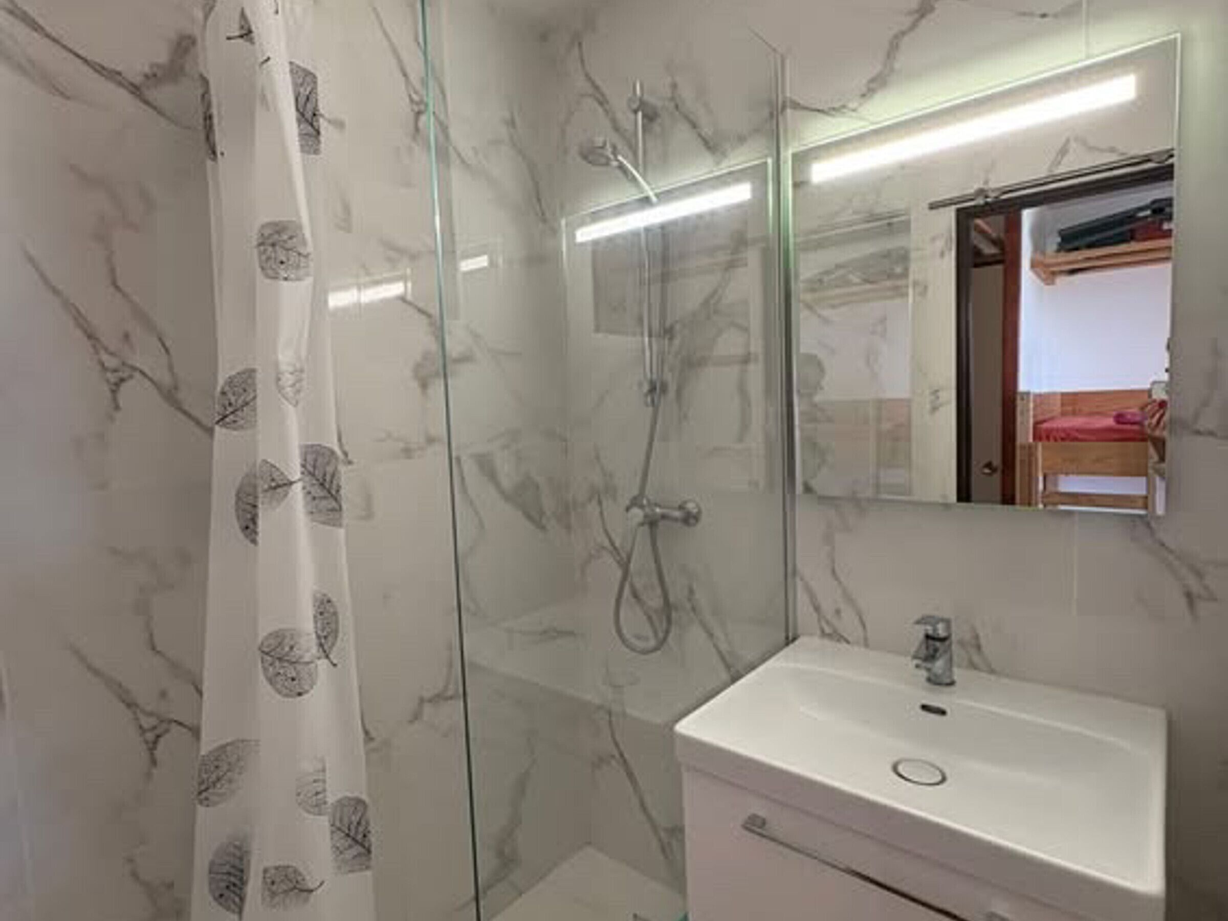 Casa de banho com cabine de duche em vidro, lavatório branco e espelho sobre o lavatório.