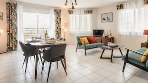 A modern living room with a dining area, a sofa set, a television, and a view of the city.