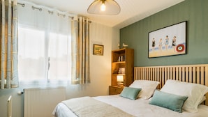 A neatly arranged bedroom with a large bed, a bedside table with a lamp, a bookshelf, and a framed picture on the wall.