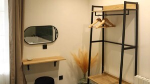 Ein kleines Zimmer mit Schreibtisch, Spiegel, Wandregal und Heizkörper.
