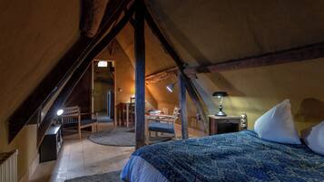 An attic bedroom with a sloped ceiling, a bed with a patterned bedspread, a desk with a chair, and a lamp.