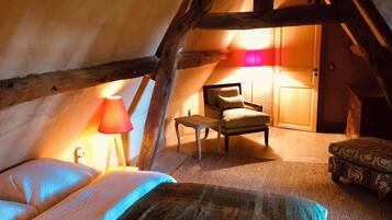 Un dormitorio acogedor en el ático, con cama, sillón, mesa y lámpara.