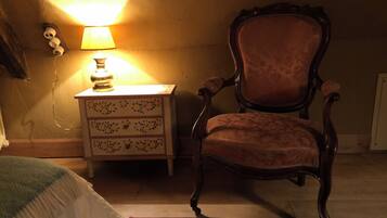 A room with a wooden chair, a bedside table with a lamp, and a patterned rug.