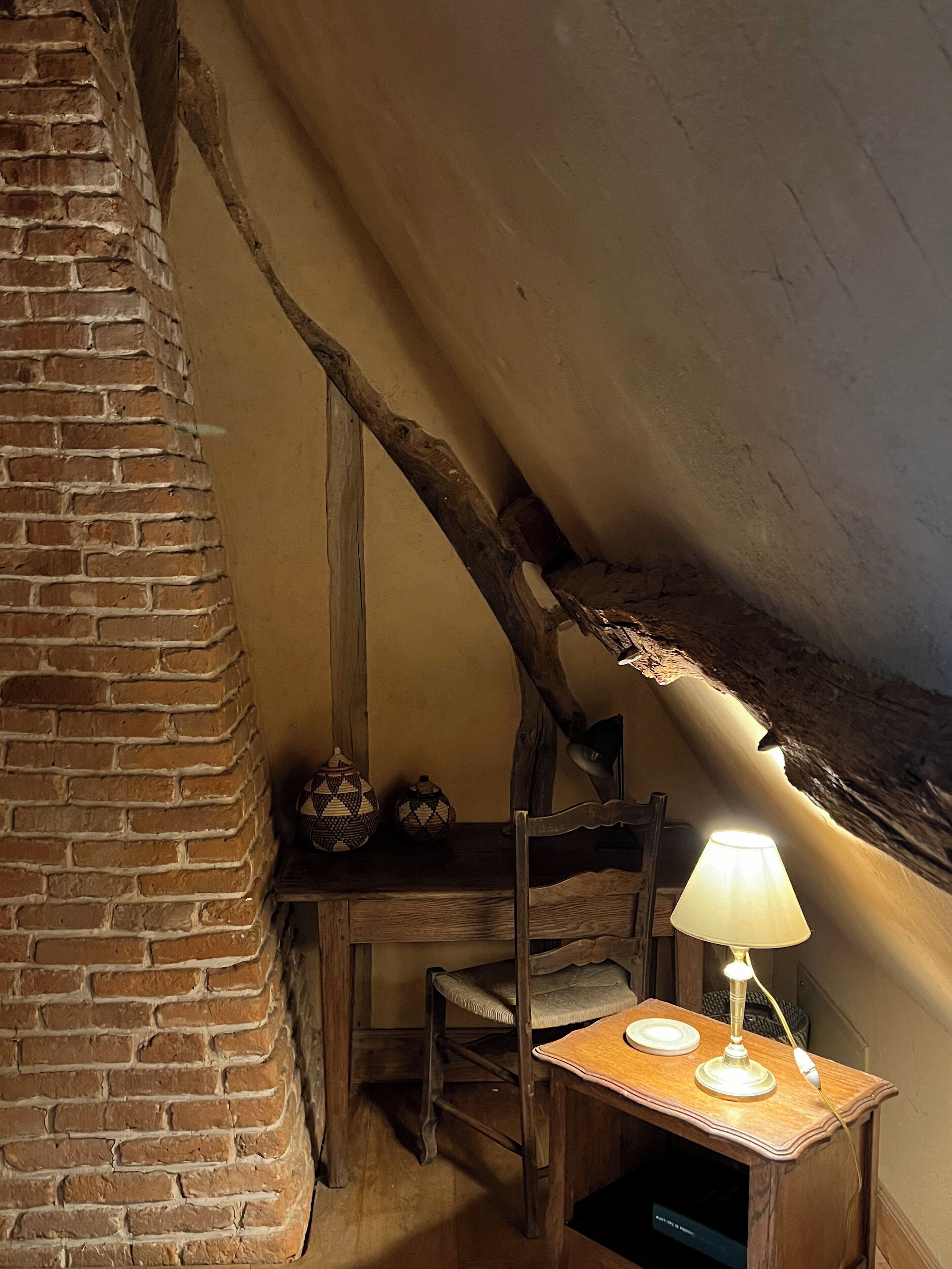 A rustic room with exposed brick walls, a wooden table with a lamp, and a chair.