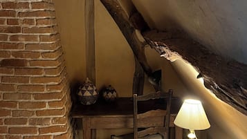 A rustic room with exposed brick walls, a wooden table with a lamp, and a chair.