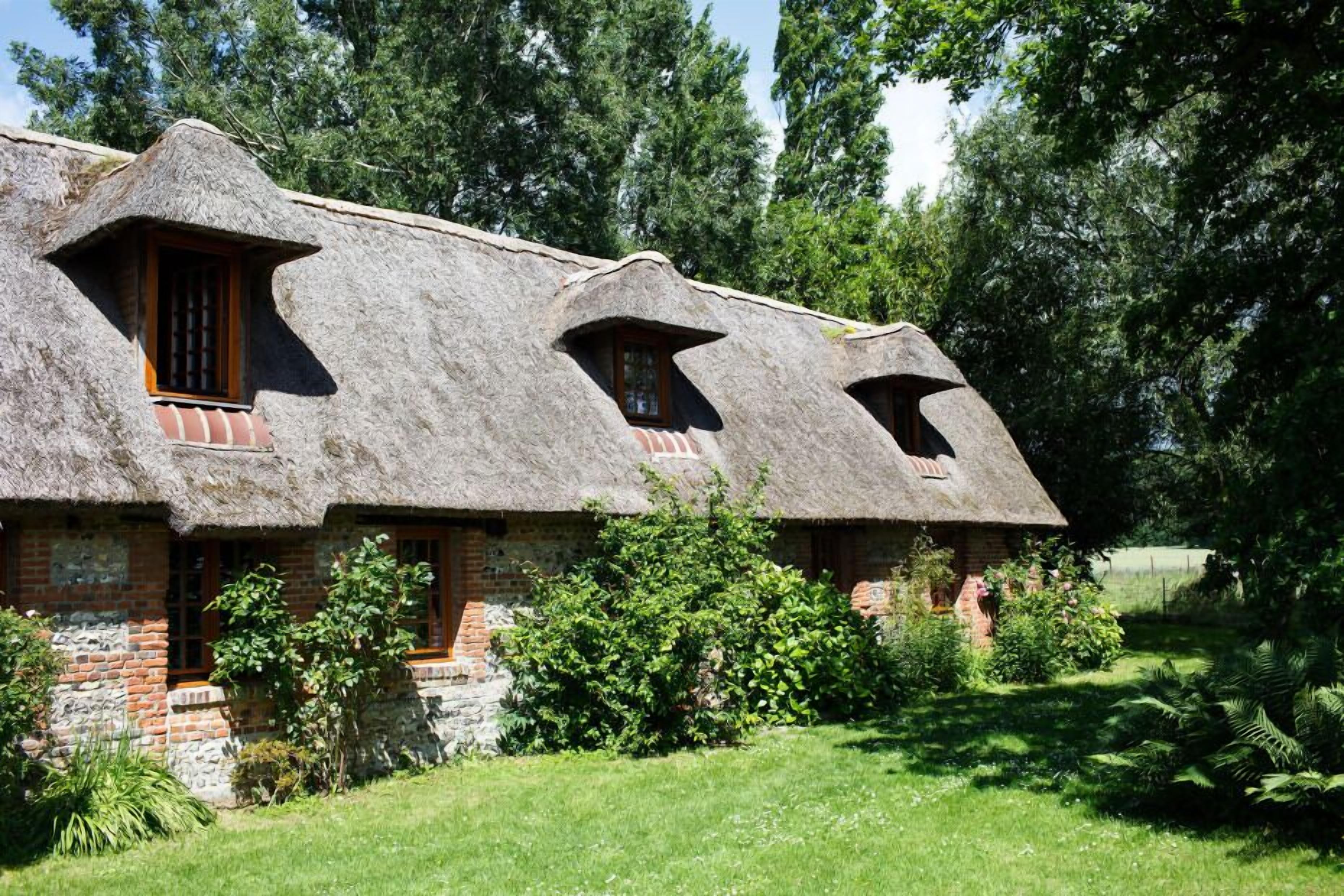 Une maison de campagne au toit de chaume, aux murs en briques et aux nombreuses fenêtres dotées de cadres en bois.