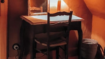 Una stanza piccola, scarsamente illuminata, con una scrivania in legno, una sedia, una lampada e uno specchio.