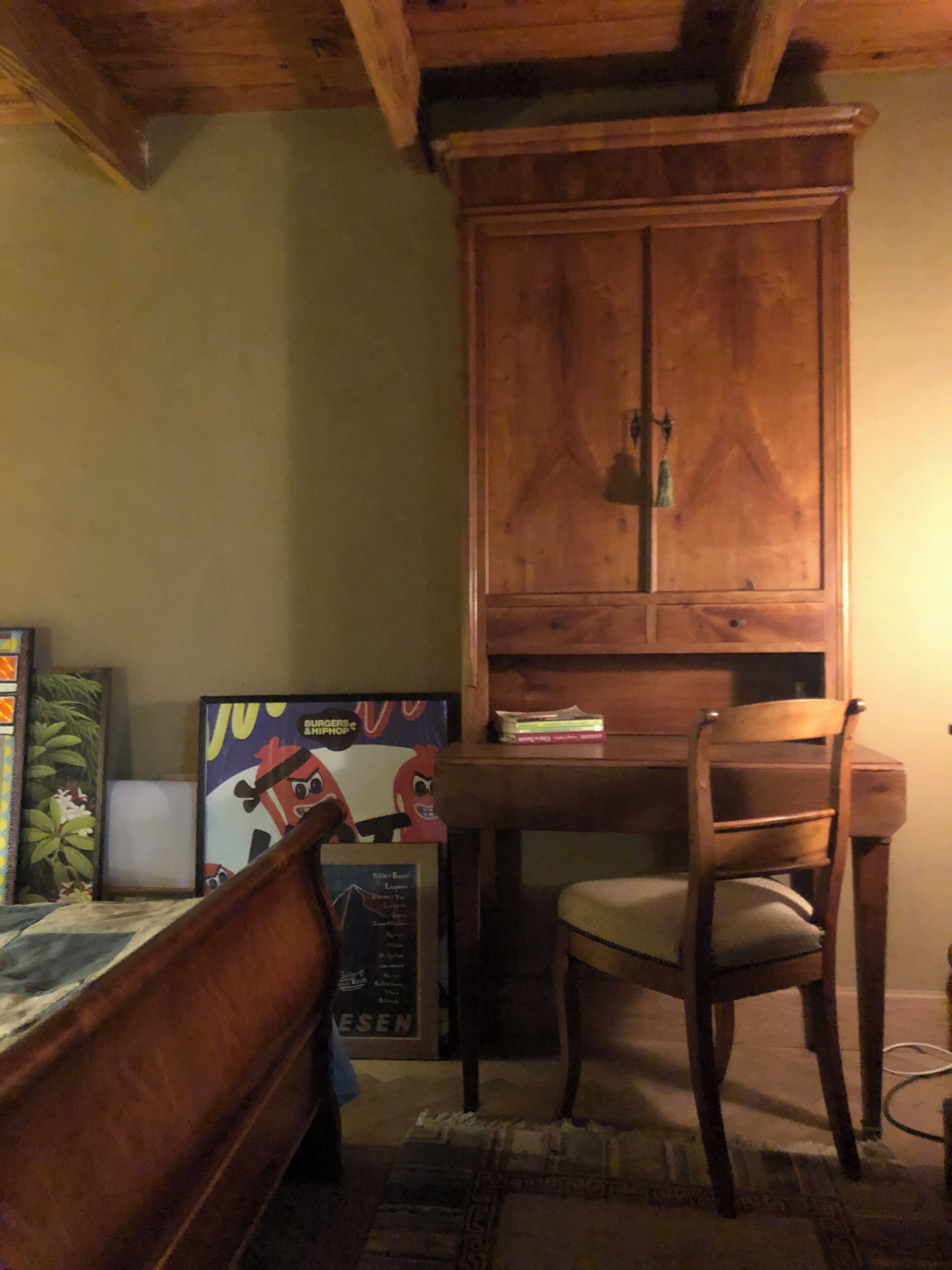 A room with a wooden cabinet, a chair, a bed, and a poster on the wall.
