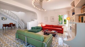 Un vaste salon avec un escalier, un canapé rouge, des fauteuils verts et un sol à motifs.