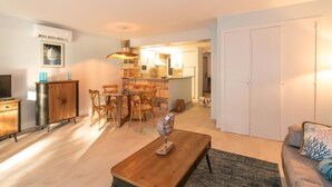 Un salon moderne avec une table basse en bois, un canapé, un coin repas avec une table et des chaises, et une cuisine en arrière-plan.