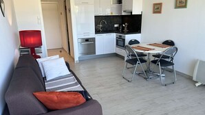A modern living room with a grey sofa, a red lamp, and a dining area with a table and chairs. - Studio for 2 in Port Camargue, sea view (Le Grau-du-Roi)
