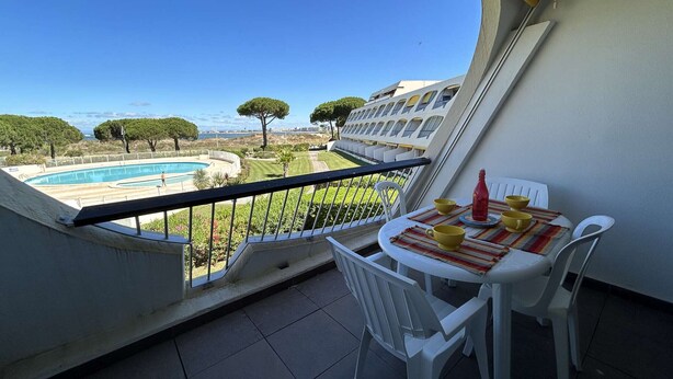 A balcony with a view of a swimming pool, a table with chairs, and a bottle. - Studio for 2 in Port Camargue, sea view (Le Grau-du-Roi)