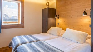 Ein Schlafzimmer mit zwei Betten, einem Fenster mit Bergblick, Holzwänden und einem Deckenventilator.
