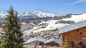 Eine Bergstadt mit schneebedeckten Gipfeln im Hintergrund, Holzhäusern und blauem Himmel.