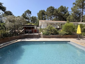 Una piscina con cubierta de madera, un pequeño espacio exterior con mobiliario y un edificio con tejado de baldosas.