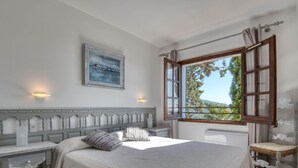 A bedroom with a large bed, a nightstand, a chair, a window with curtains, and a painting on the wall. - Modern House on the Costa Brava with Private Pool and Air Conditioning (Calonge)