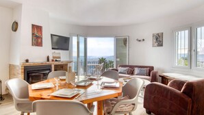 A modern living room with a dining area, a fireplace, and a large window offering a view. - Modern House on the Costa Brava with Private Pool and Air Conditioning (Calonge)