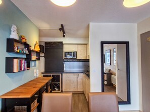 A compact kitchen with a microwave, a sink, and a refrigerator. There is a wooden dining table with chairs and a shelf with books and figurines. - Spacious apartment with parking and pool access in Flaine (Flaine)