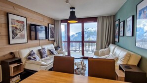 Ein gemütlicher Raum mit einer Holzwand, einem weißen Ledersofa, einem Holztisch und gerahmten Bildern.
