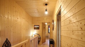 Un couloir en bois avec une rambarde en bois, un banc et une porte donnant sur une autre pièce.