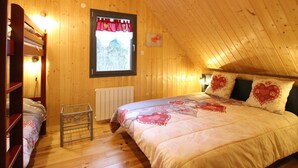 Une chambre mansardée chaleureuse, avec un lit superposé, un radiateur et une fenêtre donnant sur les arbres.