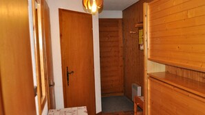 Un couloir étroit aux murs en bois, avec une porte donnant sur une autre pièce. Un banc est placé contre le mur, et on peut voir un luminaire suspendu au plafond.