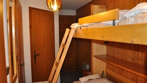 Une chambre avec un lit superposé, une échelle, des murs en bois, une porte et un luminaire suspendu.