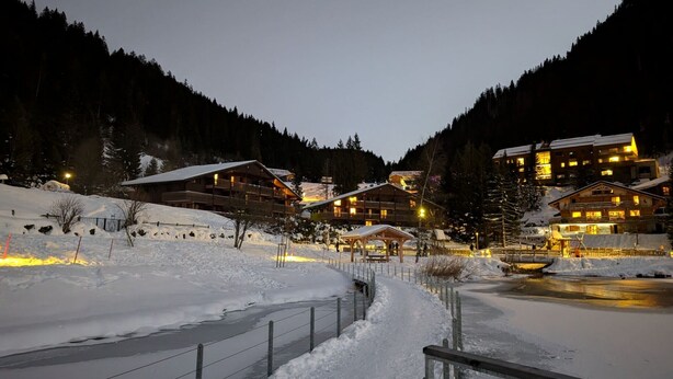 Une station de ski enneigée, avec plusieurs bâtiments en bois, un sentier bien dégagé et un paysage montagneux en toile de fond.