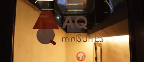 Et hotelinteriør med et synligt logo 'AQ miniSUITES' og et skilt med 'rygning forbudt'.