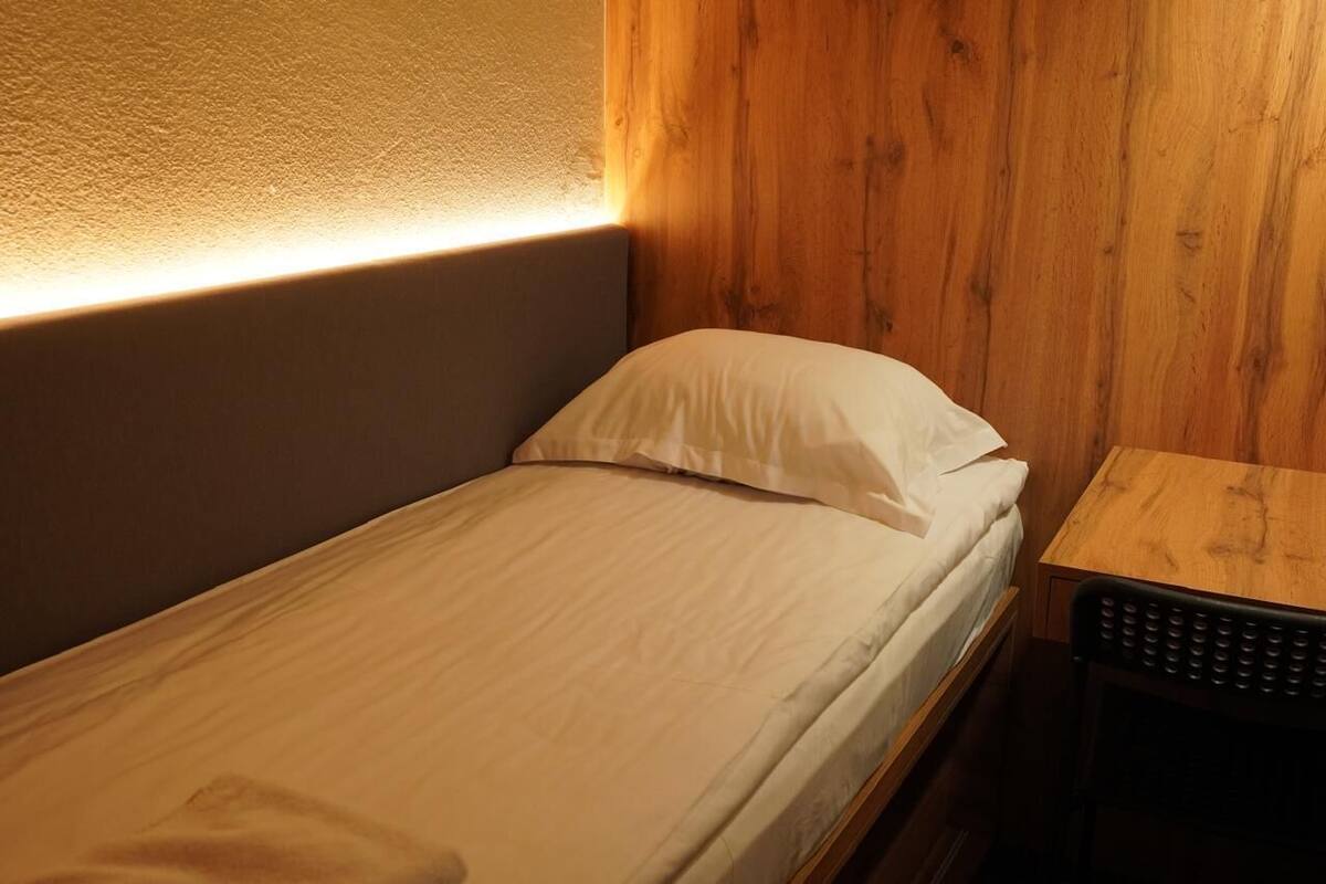 A small, single-bed room with a wooden headboard and a small table beside the bed.