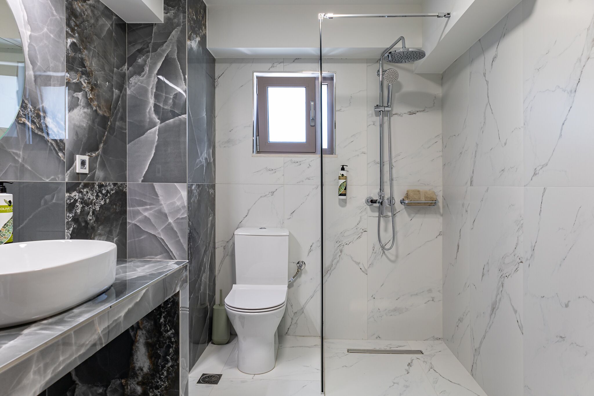 Ein modernes Badezimmer mit Marmorwaschtisch, Toilette, einer Duschkabine und einem kleinen Fenster.