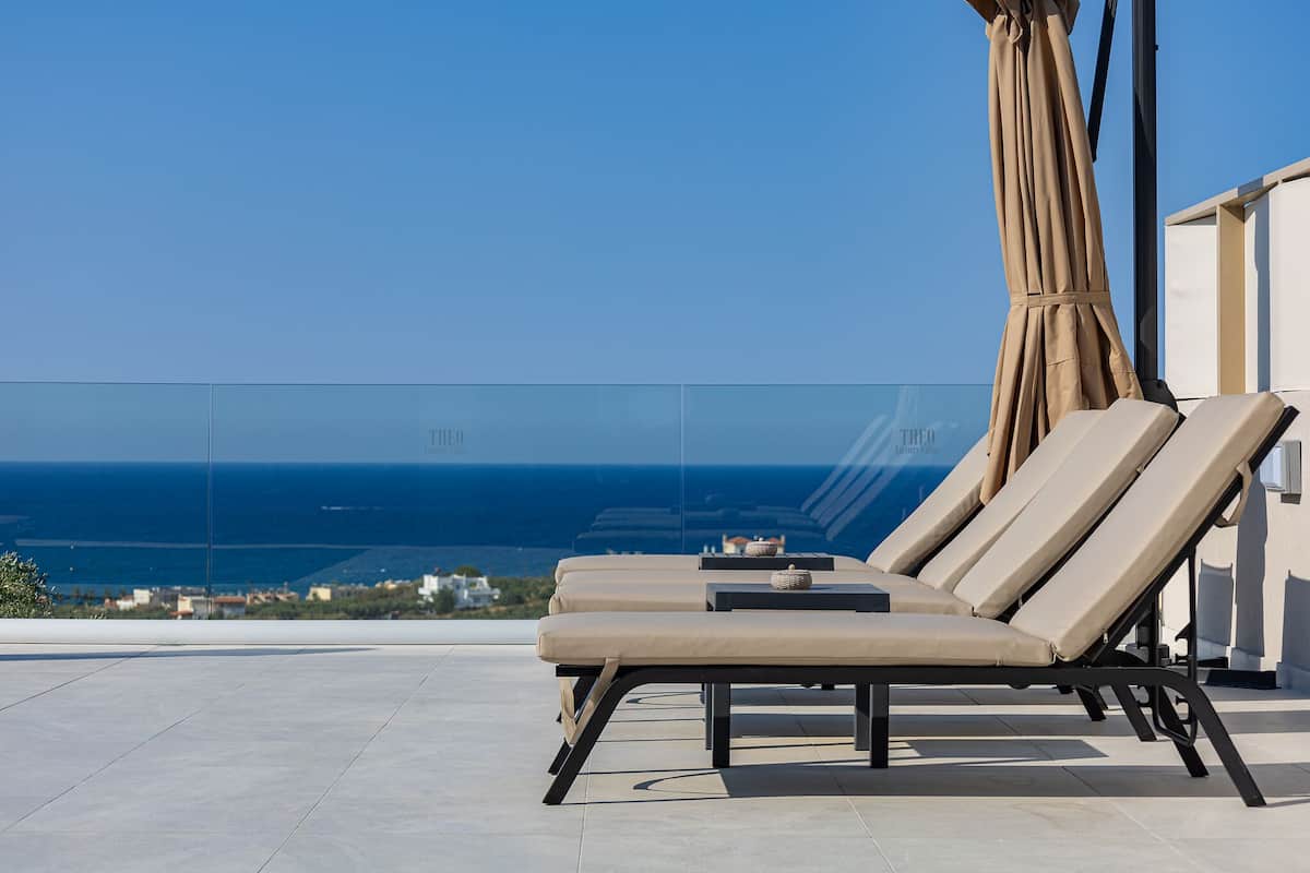 A rooftop terrace with three lounge chairs and a table, overlooking a coastal view.