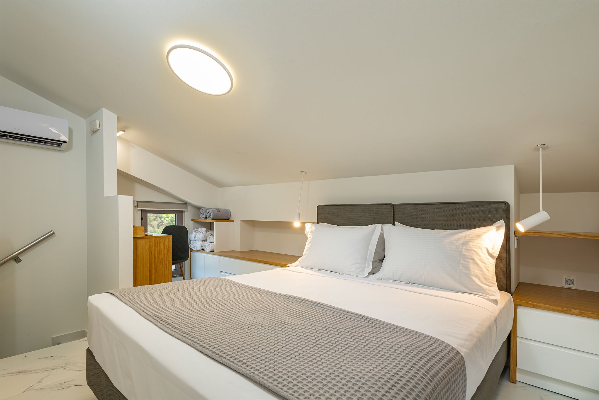 Ein modernes Schlafzimmer mit einem großen Bett, einem Nachttisch, einem Schreibtisch und einer Klimaanlage.