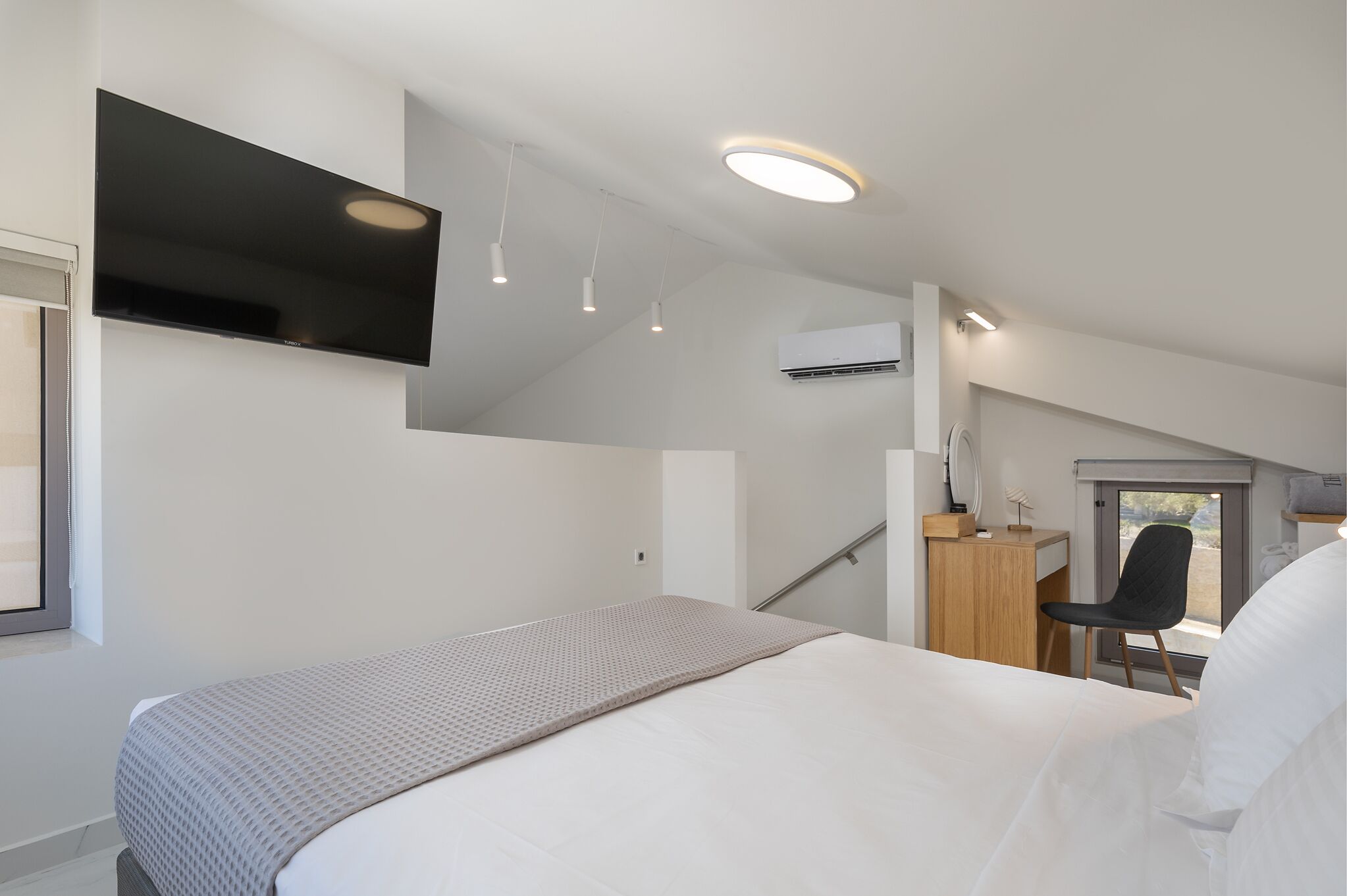 A modern hotel room with a bed, a desk, a chair, and a TV.