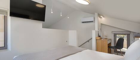 A modern hotel room with a bed, a desk, a chair, and a TV.