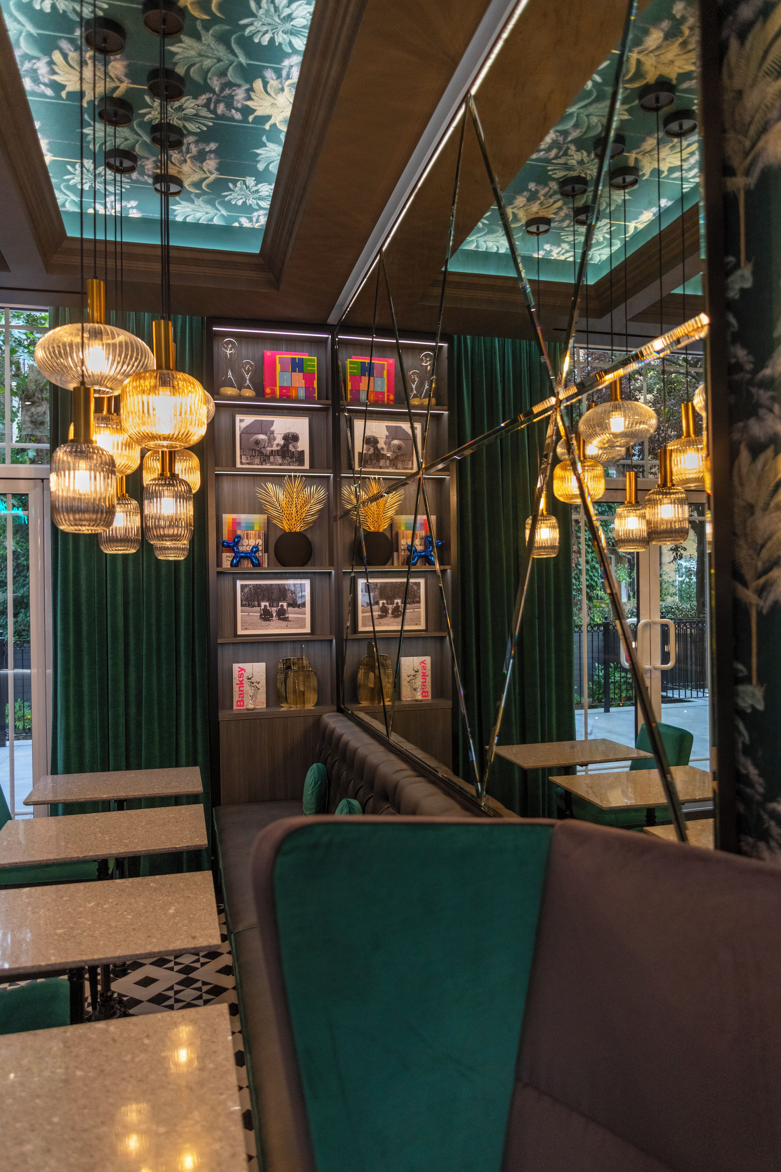 Ein Restaurantinneres mit grünen Samtvorhängen, einer Sitzgruppe mit gepolsterten Bänken und hängenden Pendelleuchten.