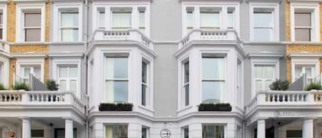 A symmetrical building facade with multiple windows, a central entrance with a sign, and a small balcony with plants.
