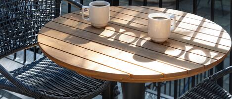 A round wooden table with two white mugs on it, surrounded by wicker chairs.